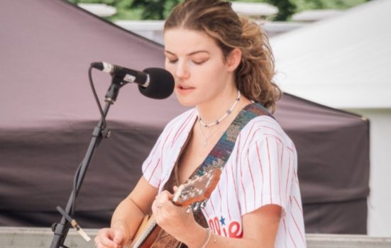 A young woman playing guitar and singing into a microphone
