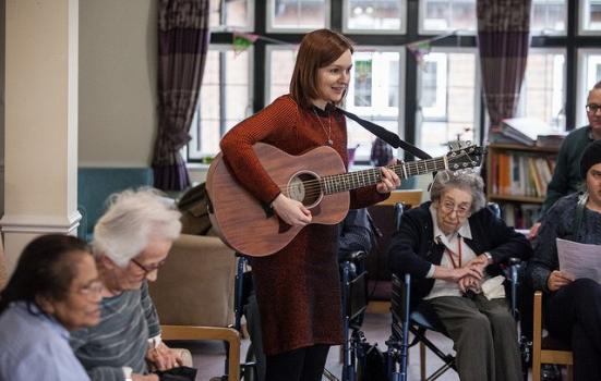 Photo of female guitarist performing in room of older people
