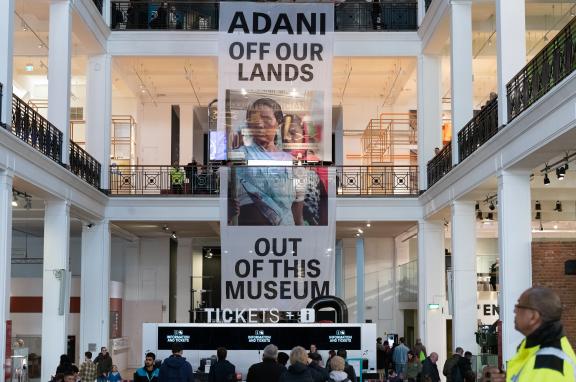 Protesters unfurl a 12-metre banner spanning the full height of the Science Museum's Energy Hall reading ‘Adani off our lands and out of this museum'