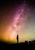 silhouette of a person looking up at a coloured starry sky